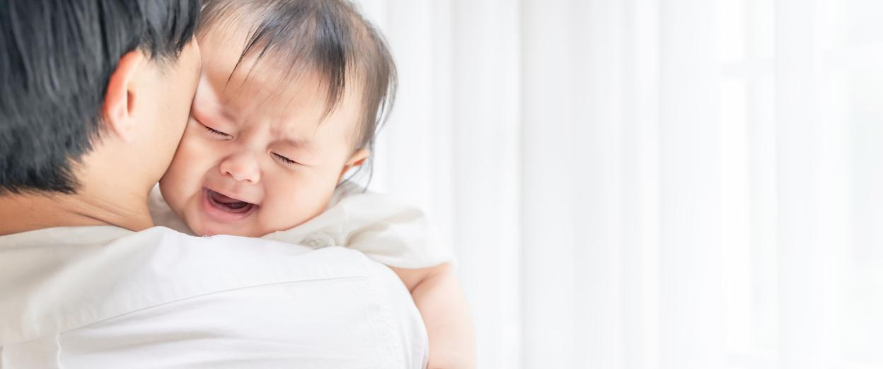 Tired 4 month old baby cries on dad's shoulder
