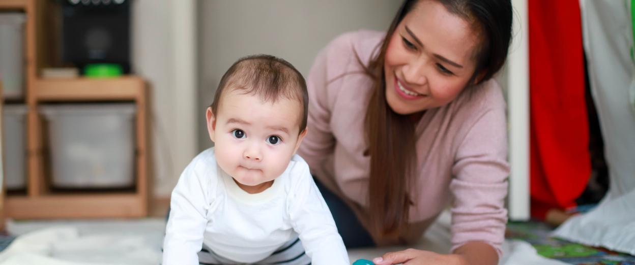 baby on hand and knees with mom behind smiling at baby