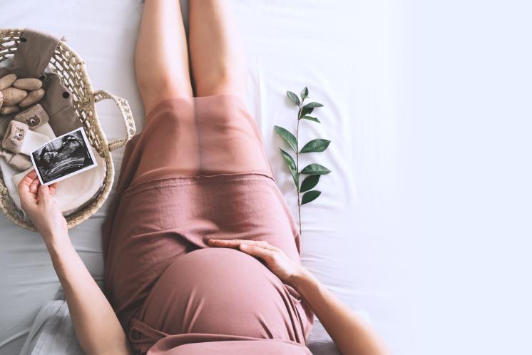 an expectant mother sitting on the floor holding her stomach, while looking at an ultrasound picture and new baby iteams