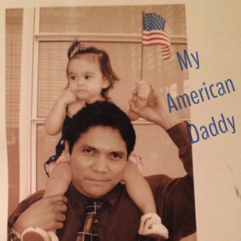 dad holding toddler on shoulders with an American flag in hand