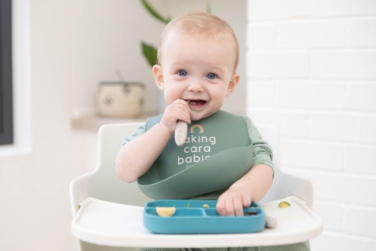 happy baby sitting in high chair with bib self feeding