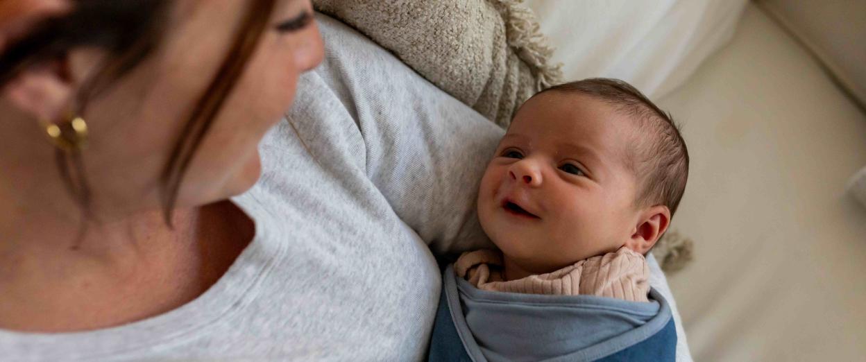 happy swaddled baby in mom's arms