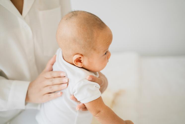 Light and bright white image of parent attempting to burp a young baby.