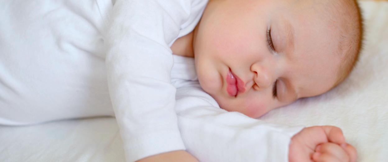 Sleeping baby on side in crib with arms extended