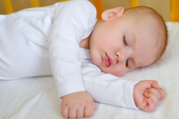 Sleeping baby on side in crib with arms extended