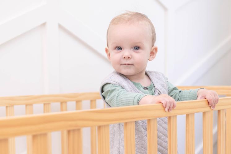 baby standing happily in crib wearing sleep sack