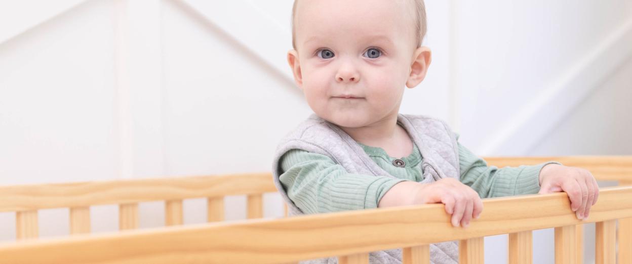baby standing happily in crib wearing sleep sack