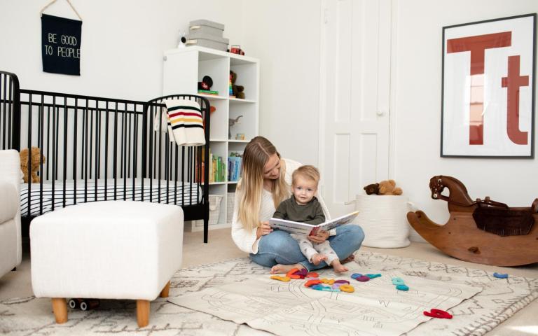 mom sitting in the middle of the nursery floor with toddler in her lap reading a book before nap time