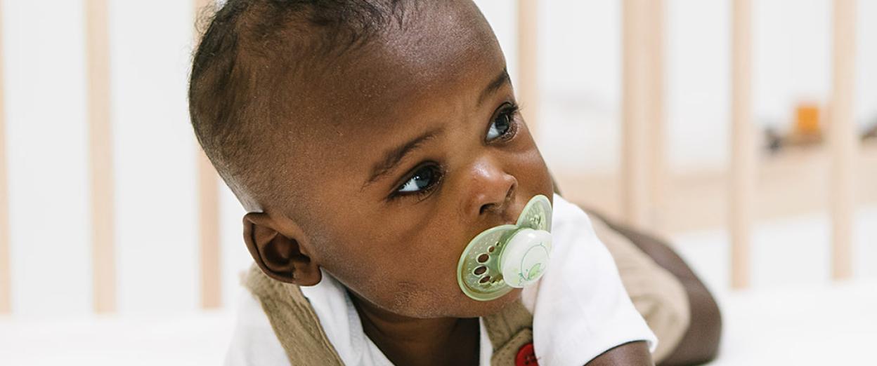five month old on tummy in crib with pacifier looking around the room