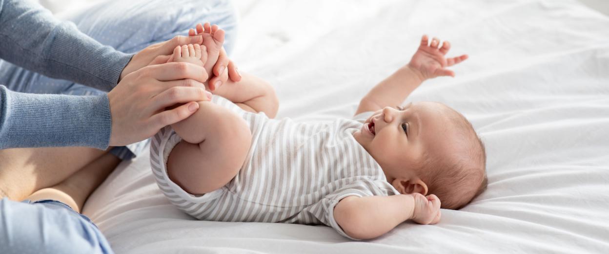 awake baby laying on white bed with parent doing exercises to relieve gas before bed