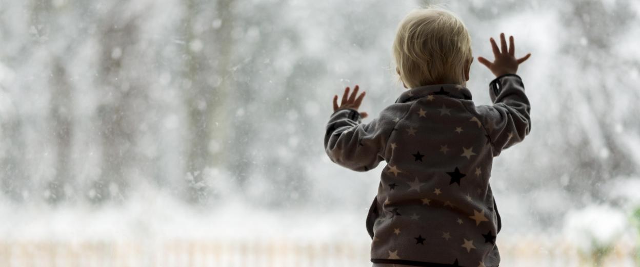 toddler dressed warmly looking out window at the snow