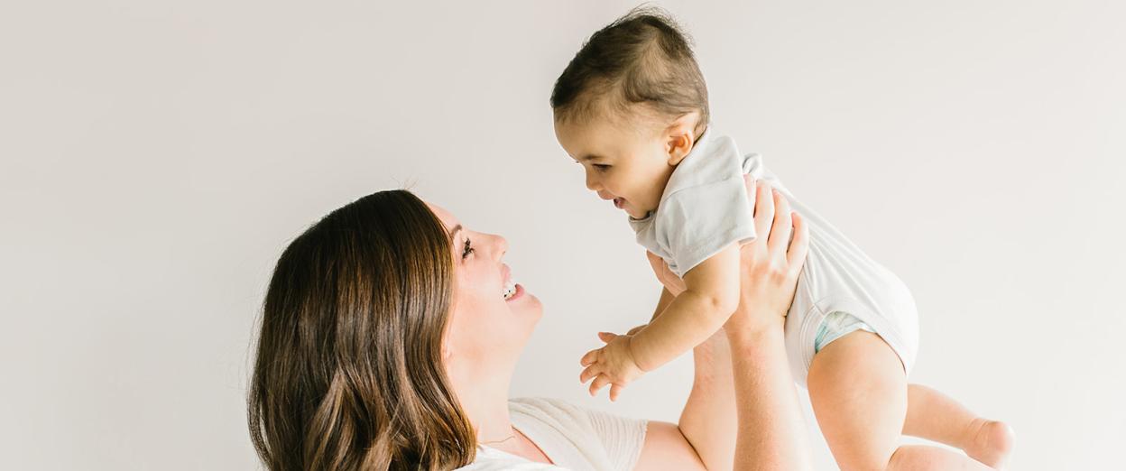 smiling mom holding smiling baby up above her