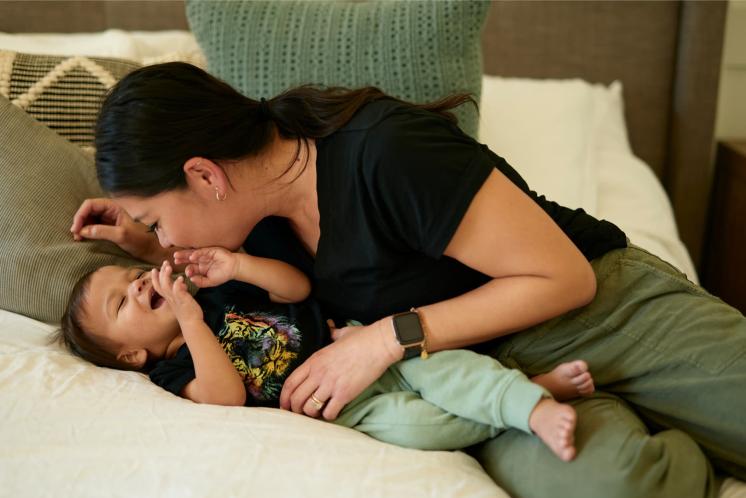 mom with older baby playfully sitting on a bed