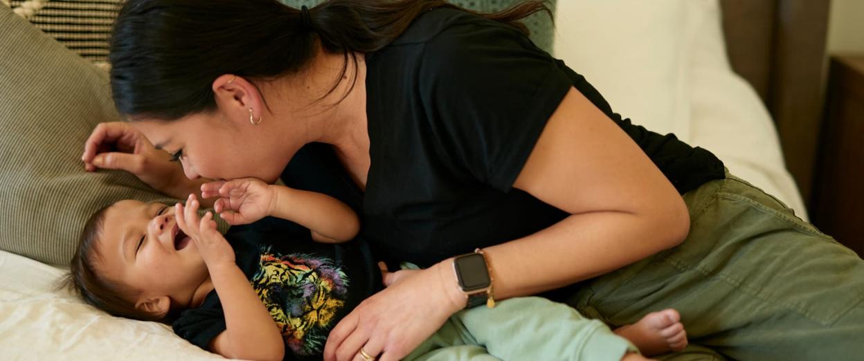 mom with older baby playfully sitting on a bed
