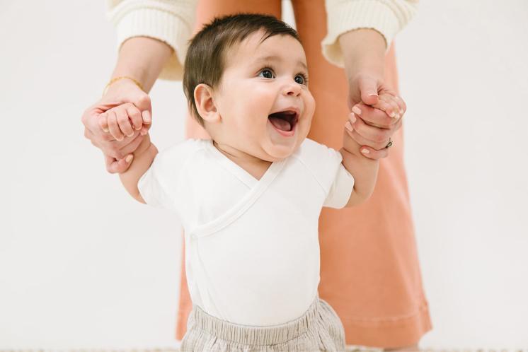 happy toddler working on learning to walk by holding mom's hands
