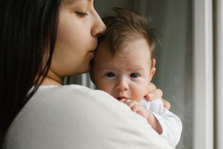 Mom kissing newborn's head on her shoulder after baby took a short nap
