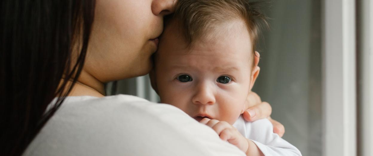 Mom kissing newborn's head on her shoulder after baby took a short nap