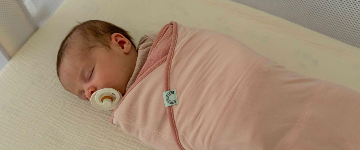 newborn swaddled with a pacifier sleeping in a bassinet