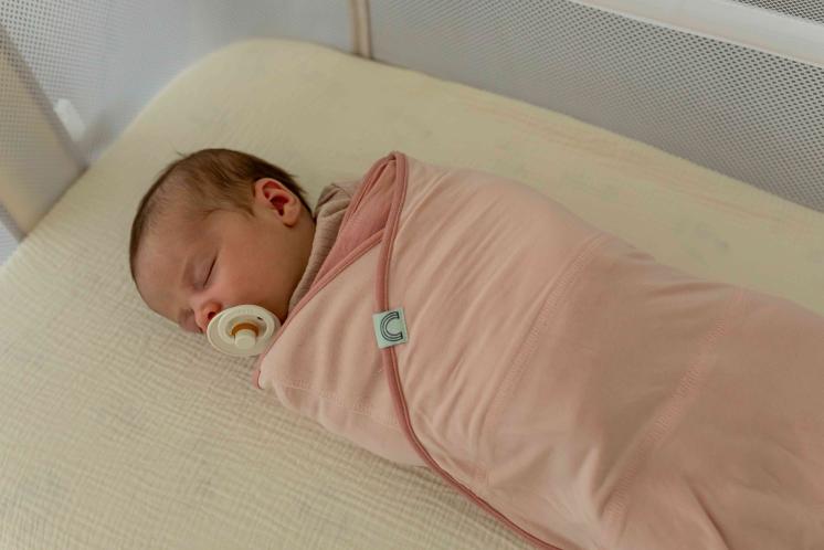 newborn swaddled with a pacifier sleeping in a bassinet