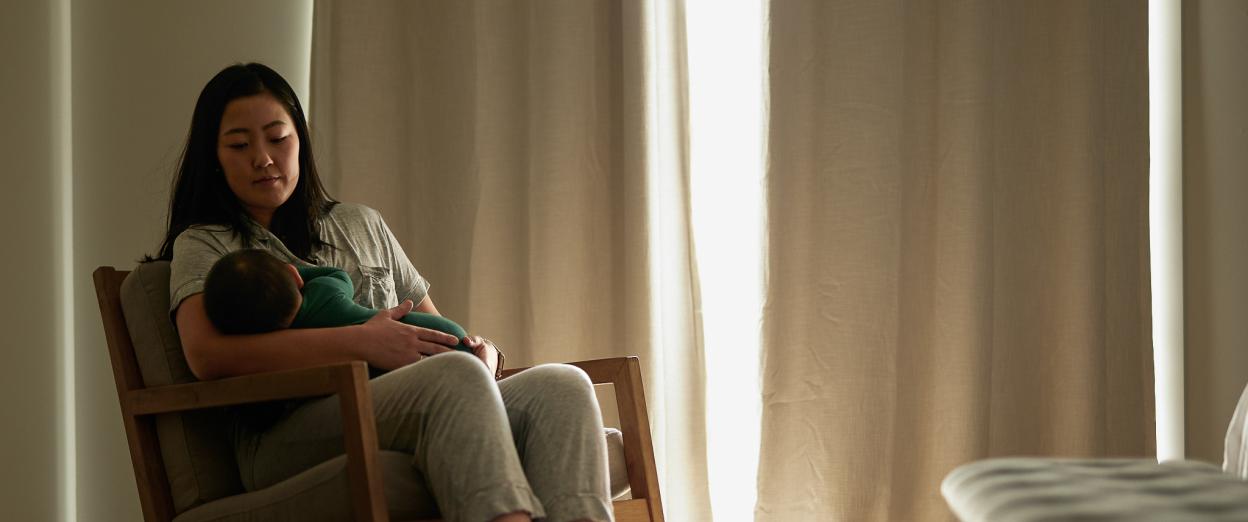 Mother sitting in a rocking chair in a dimly lit room while giving her baby a bedtime feeding.
