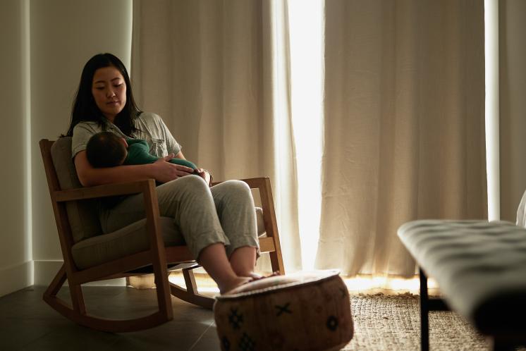 Mother sitting in a rocking chair in a dimly lit room while giving her baby a bedtime feeding.