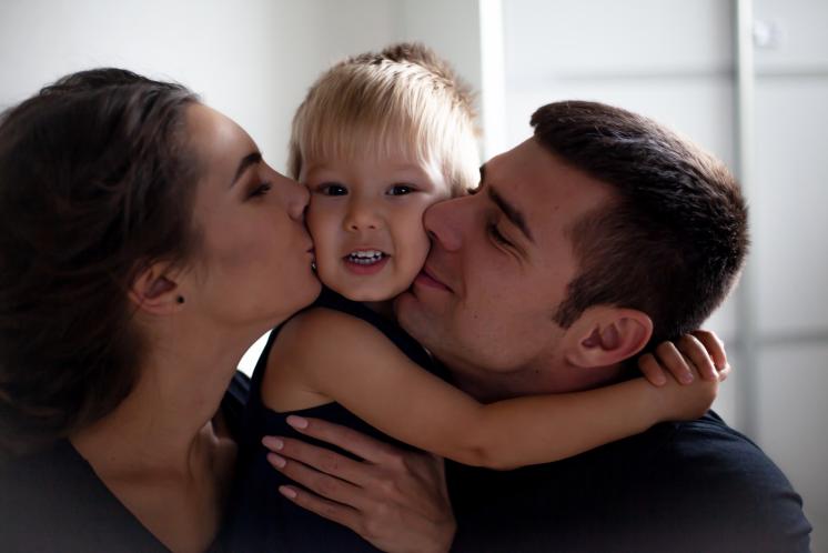 up close shot of a mom and dad kissing opposite cheeks of toddler