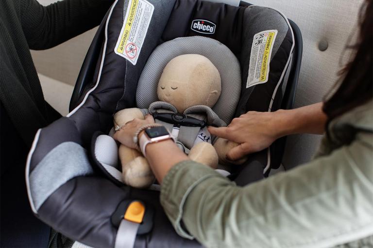 mom's hands checking the fit on a doll in car seat to practice before baby arrives