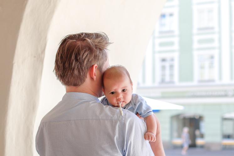 man facing away from camera with baby on his shoulder who is facing the camera as baby spits up over Dad's shoulder
