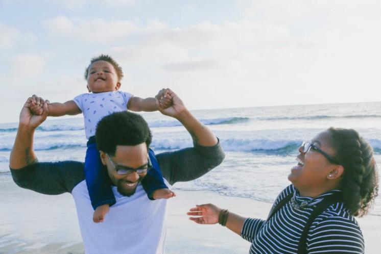 young family at the beach with baby on dad's shoulders, mom and dad smiling happily