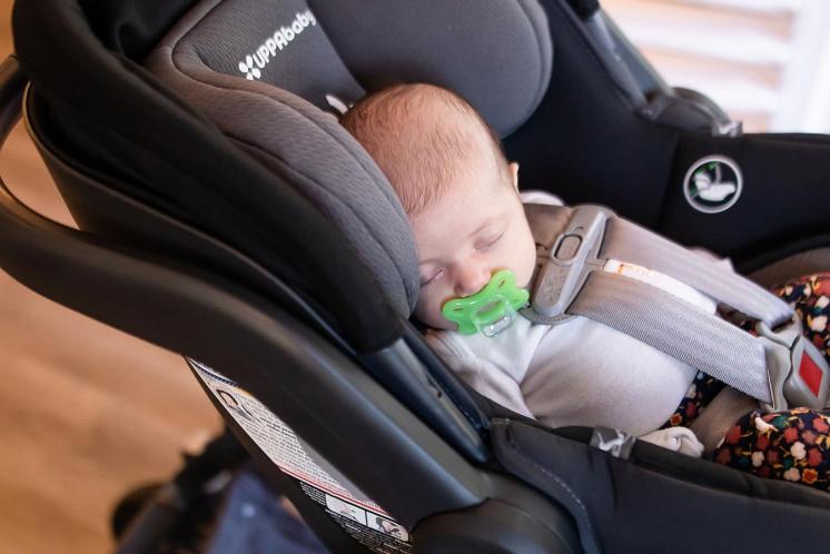 newborn baby safely sleeping in car seat with pacifier