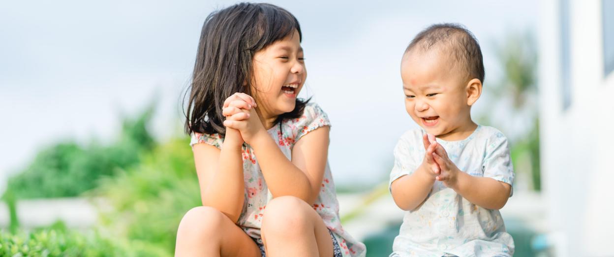 Baby brother laughing with big sister sitting on the porch after school