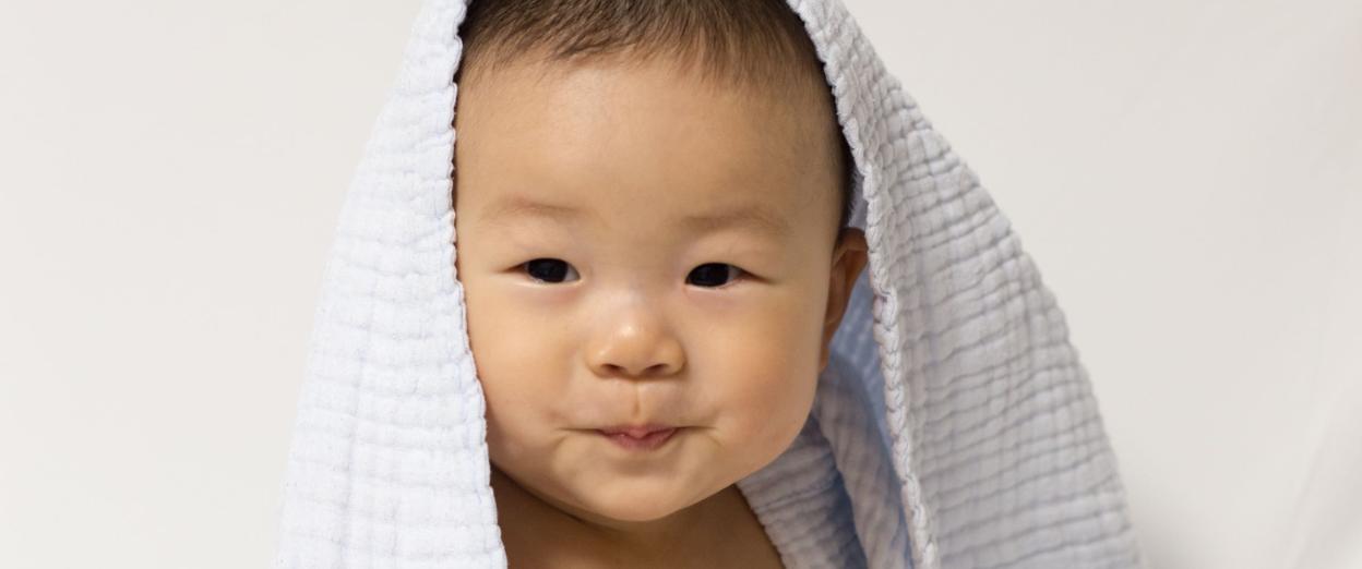 six month old baby sitting up independently playing with toys with a blue blanket on his head