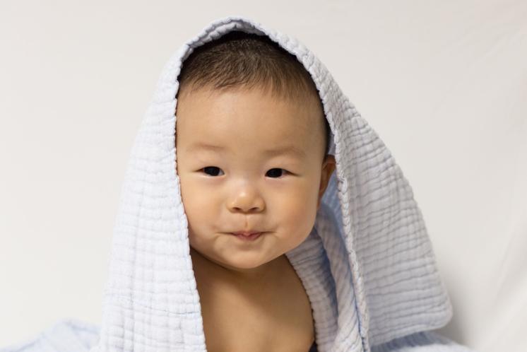 six month old baby sitting up independently playing with toys with a blue blanket on his head