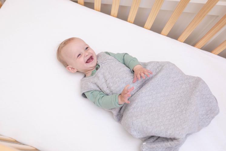 baby in crib smiling wearing a sleep sack