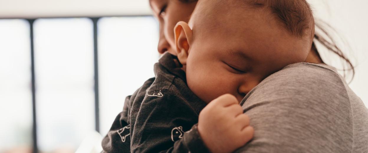 Sleeping baby being held by mom, up on shoulder, in a well lit room