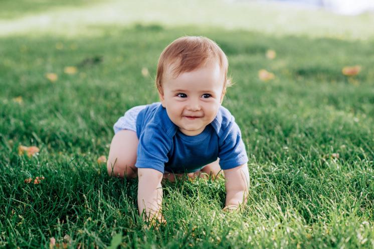 baby crawling through spring green grass wearing blue shirt and shorts
