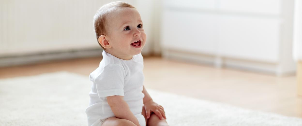 Baby wearing white onesie baby sitting up happily.