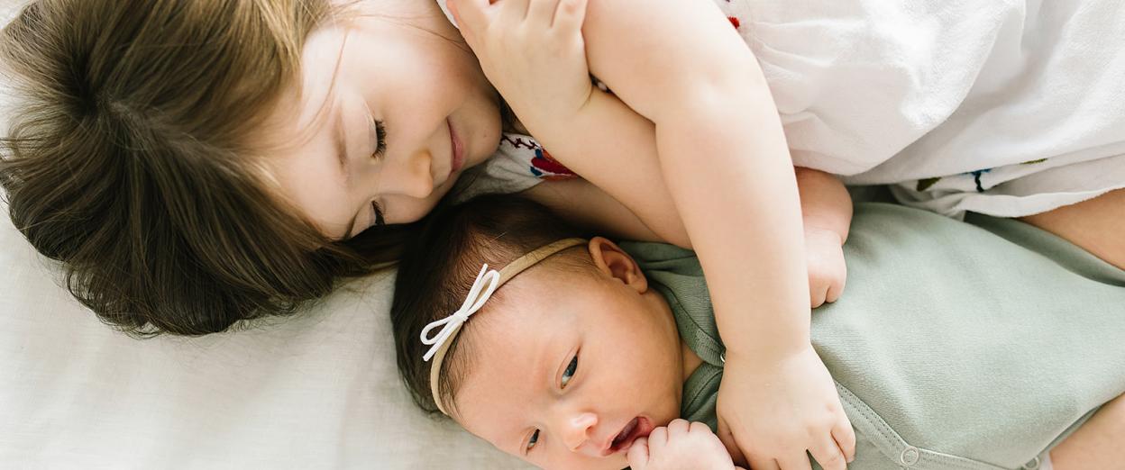 toddler girl smiling while laying with newborn sister