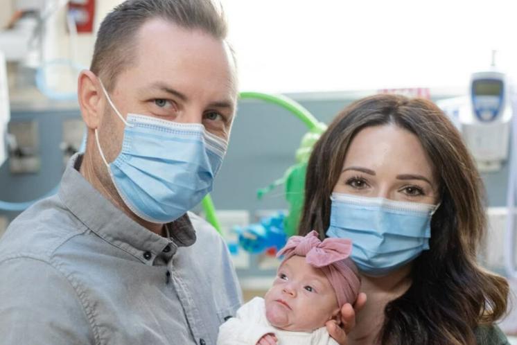 New parents with masks on holding newborn in the NICU