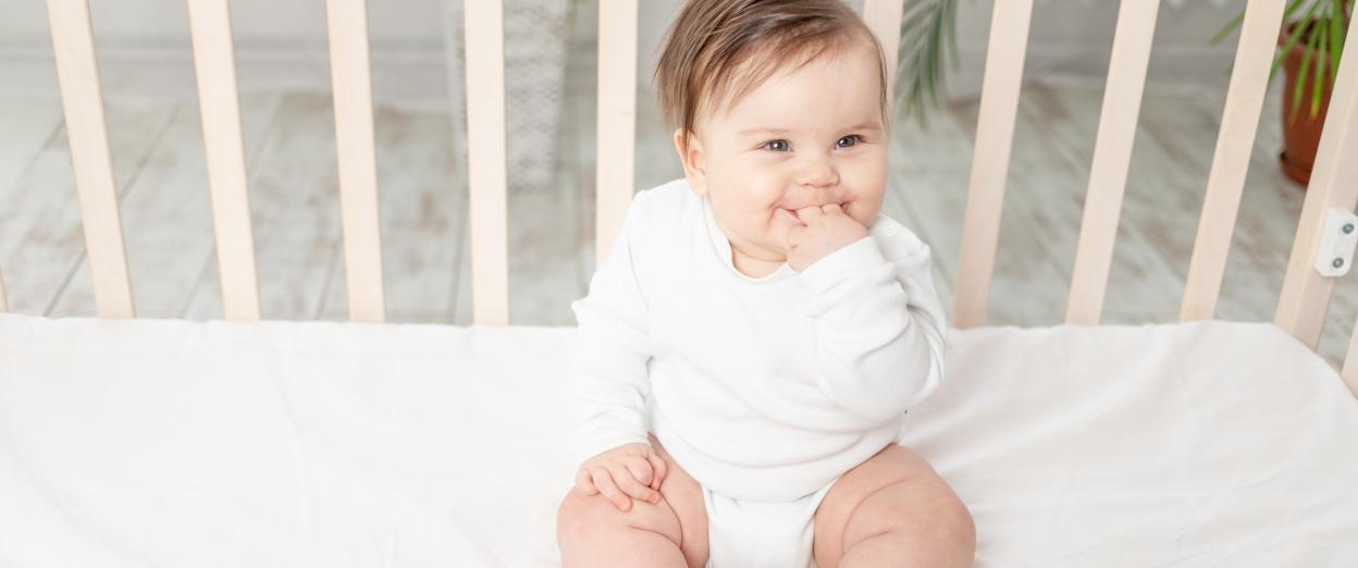 baby that just learned to sit up sitting in a crib with mattress at the lowest setting