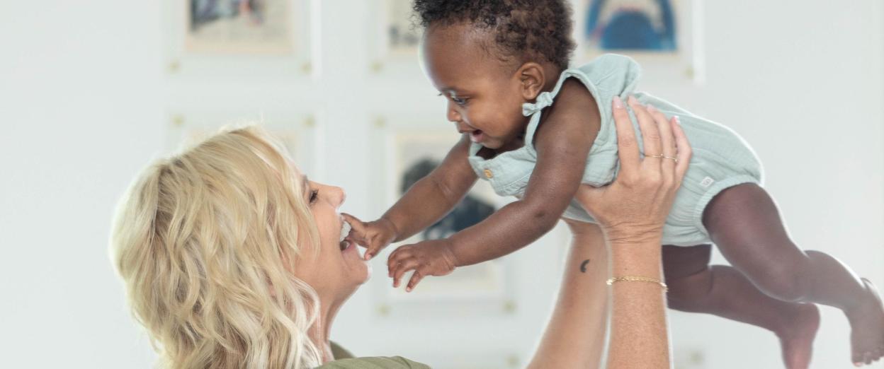 woman smiling holding baby up in front of her while baby smiles and reaches for her face