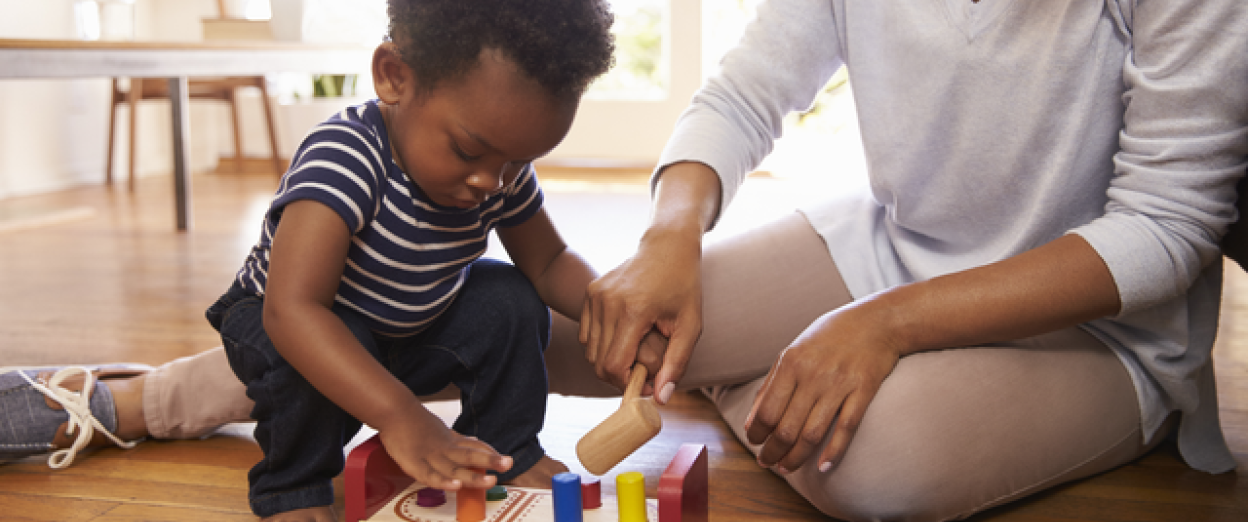 19 month old squatting down to play with peg toy with his mom on the floor
