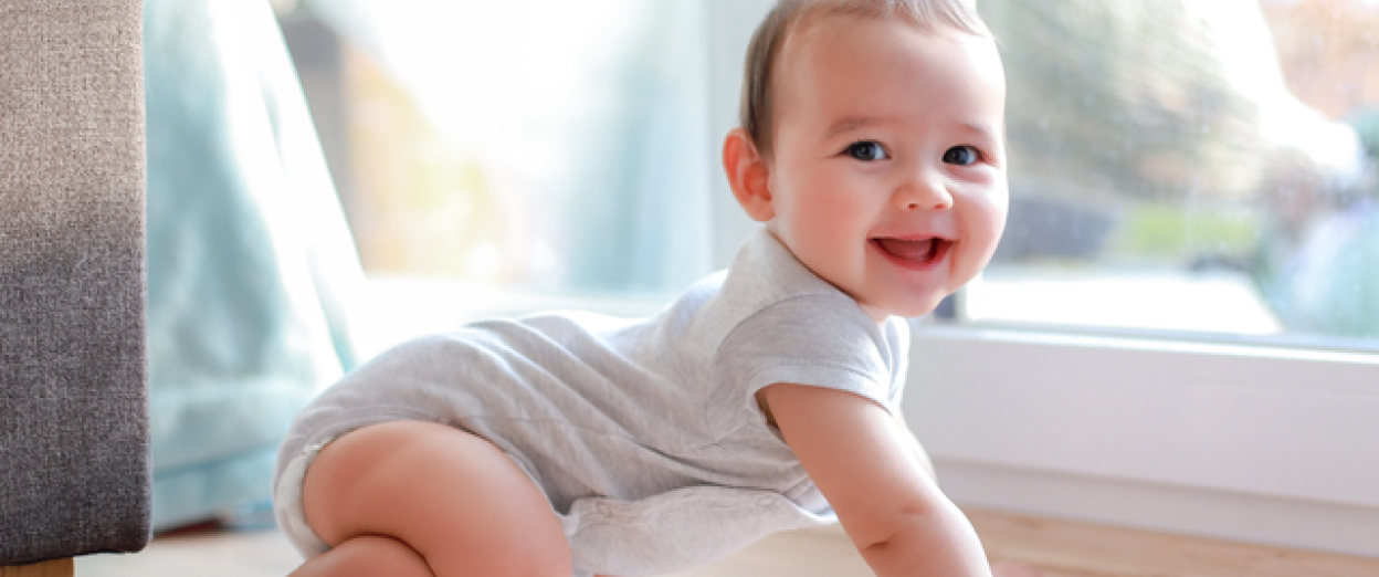 Baby smiling at camera while moving into a crawling position during a longer wake window of the 3 to 2 nap transition.