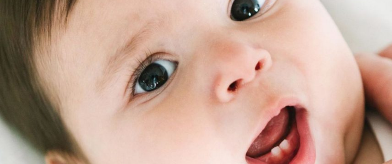 up close view of teething baby showing new bottom teeth looking at the camera